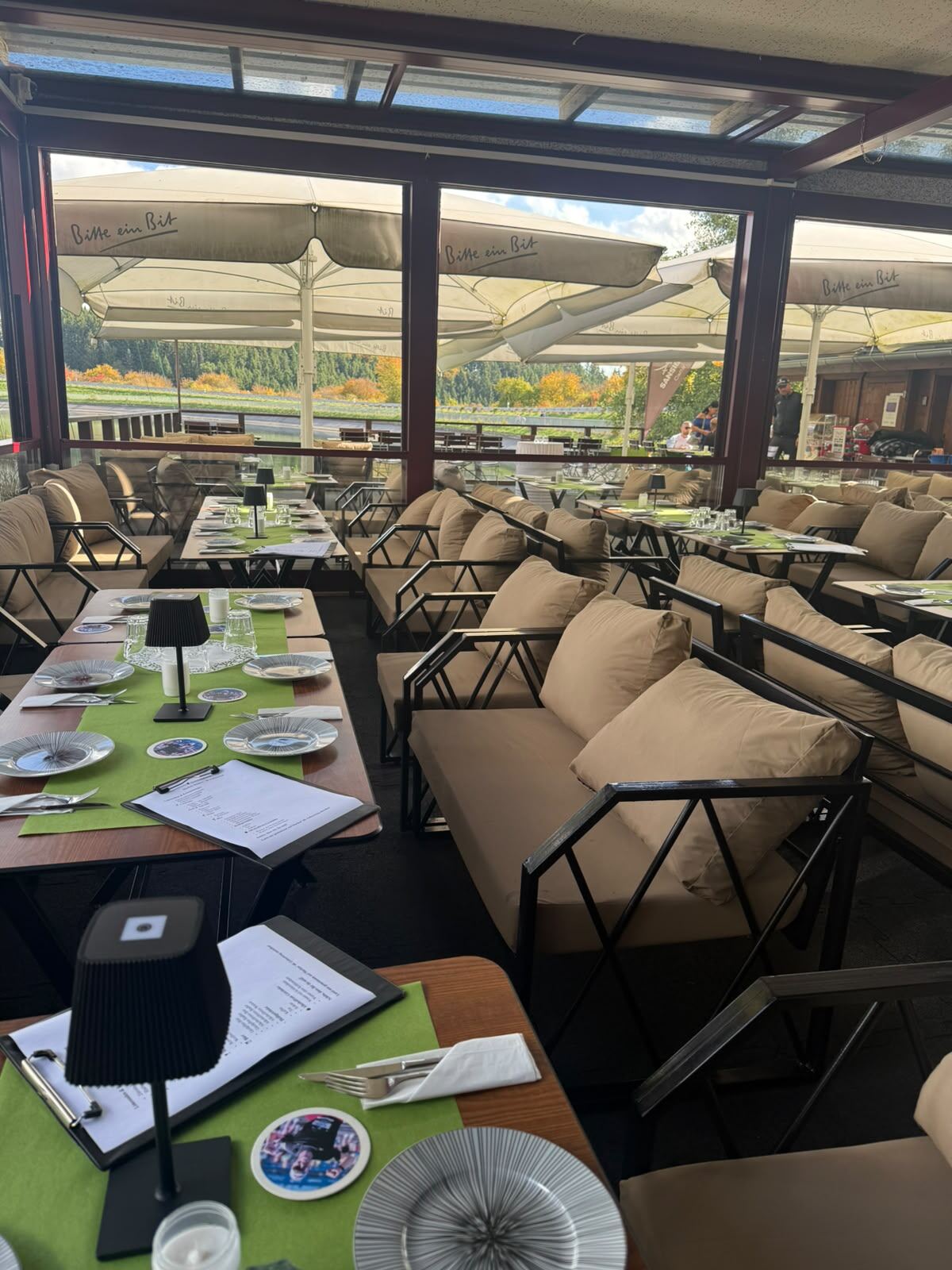 Lounge-Sitzplätze im verglasten Pavillon der Seebar, dahinter Sonnenschirme und der Freilinger See