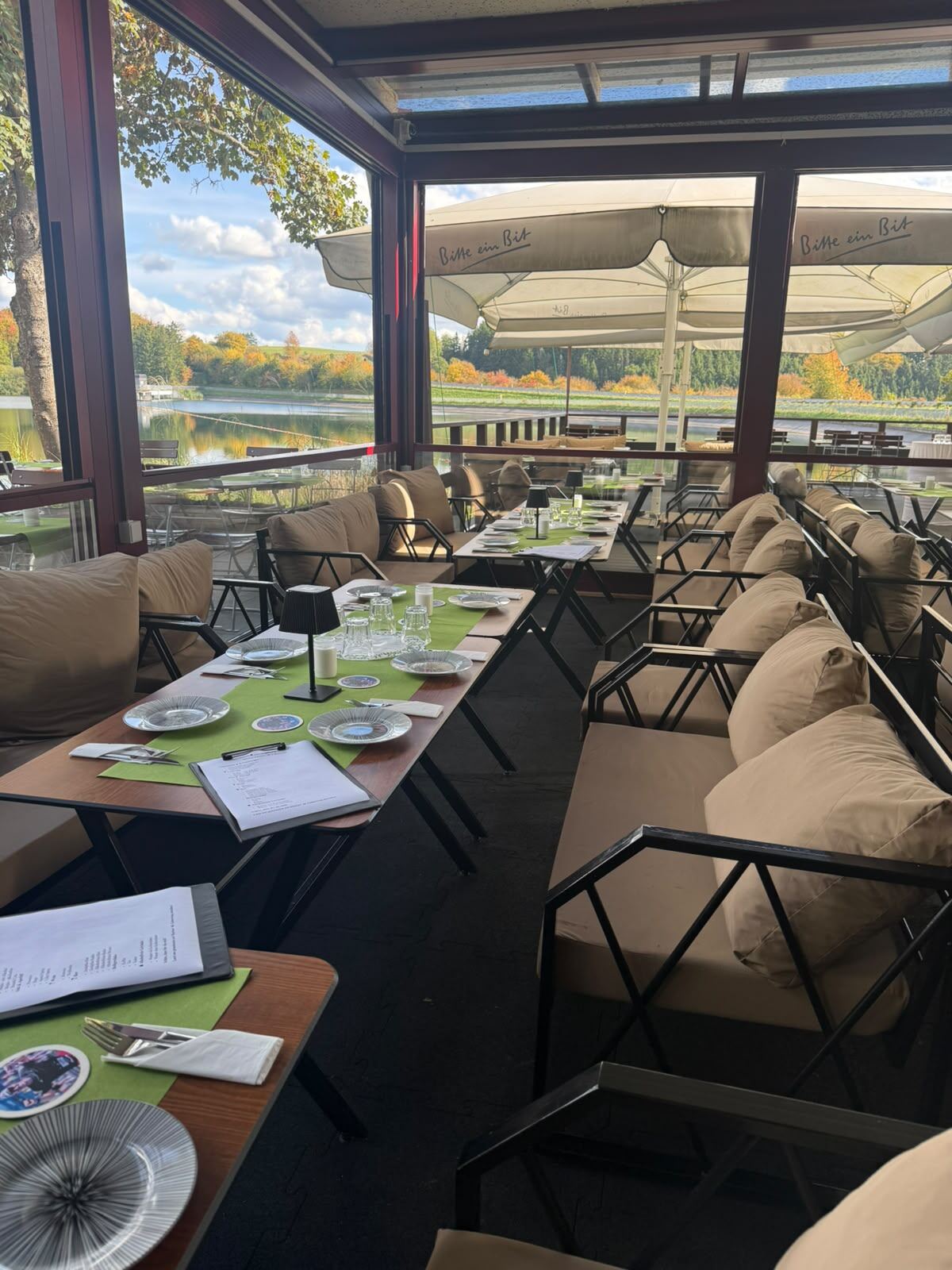 Gedeckte Tische mit Lounge-Sofas im Pavillon, durch die Fenster Blick auf den See