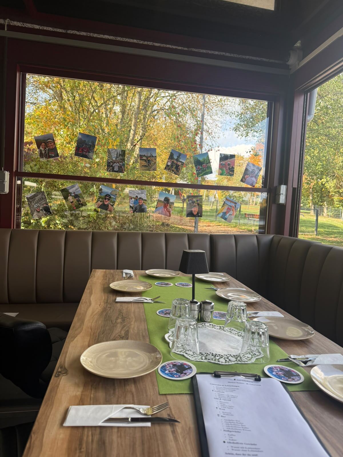 Gedeckter Holztisch an der Sitzbank, im Fenster eine Fotogirlande und Herbstbäume