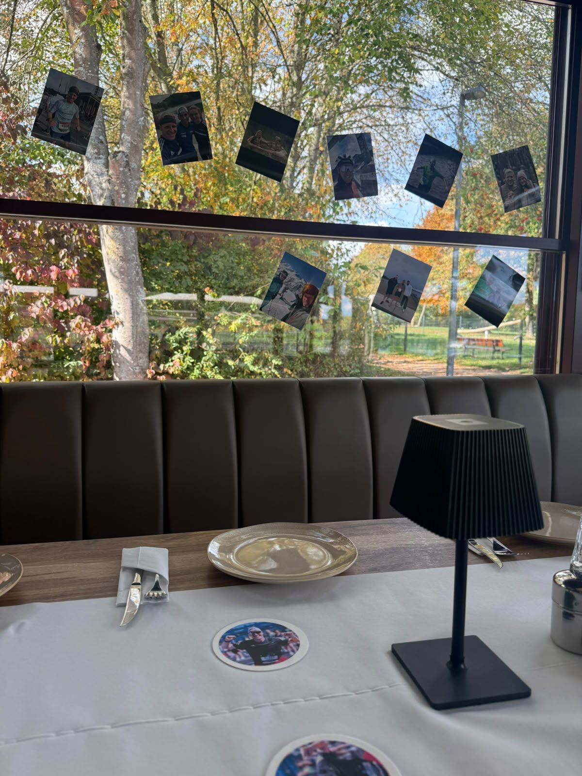 Tisch mit weißem Läufer und schwarzer Tischlampe vor großen Fenstern mit Herbstlaub